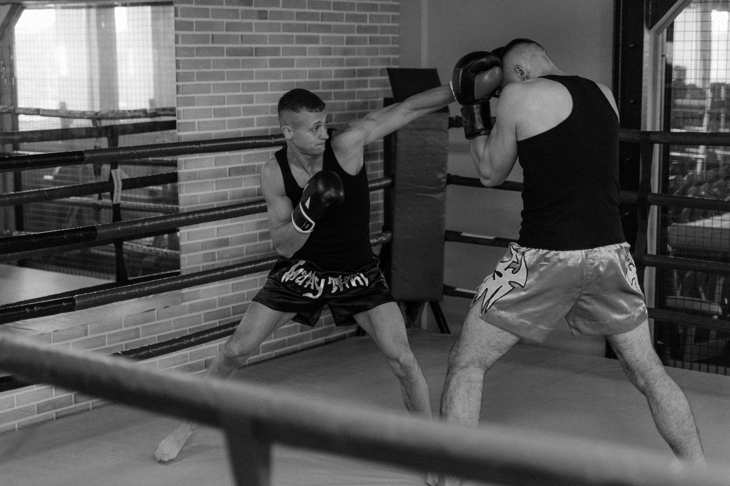 Two male boxers sparring in gym, displaying boxing skills in a monochrome setting.