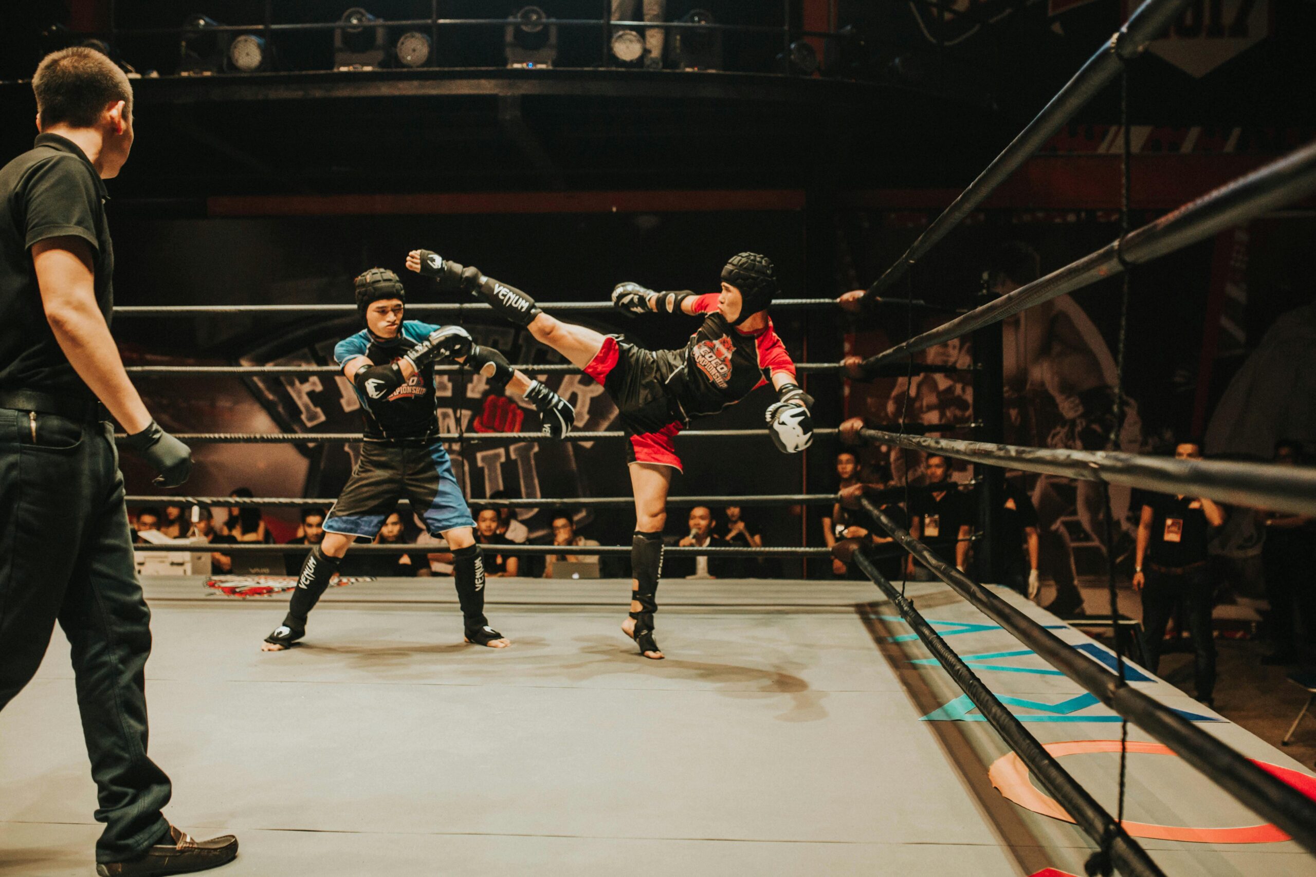 Intense kickboxing match with fighters in action inside a crowded indoor arena.