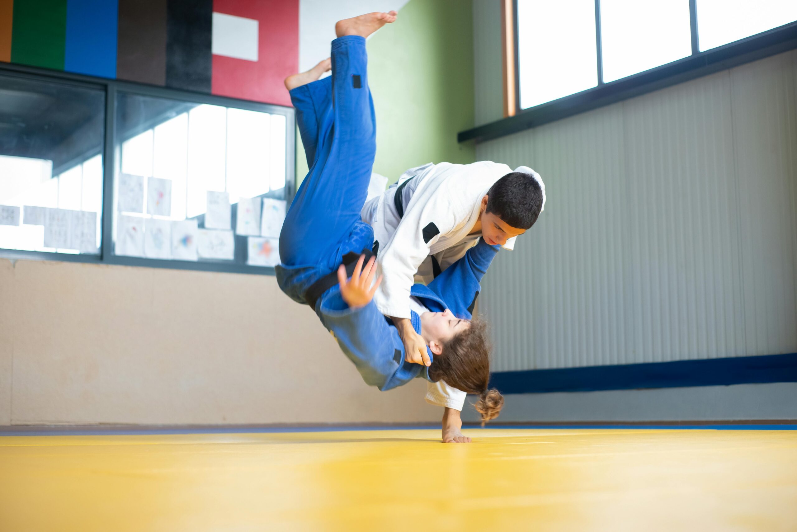 Athletes practicing a dynamic judo throw on a tatami mat indoors.