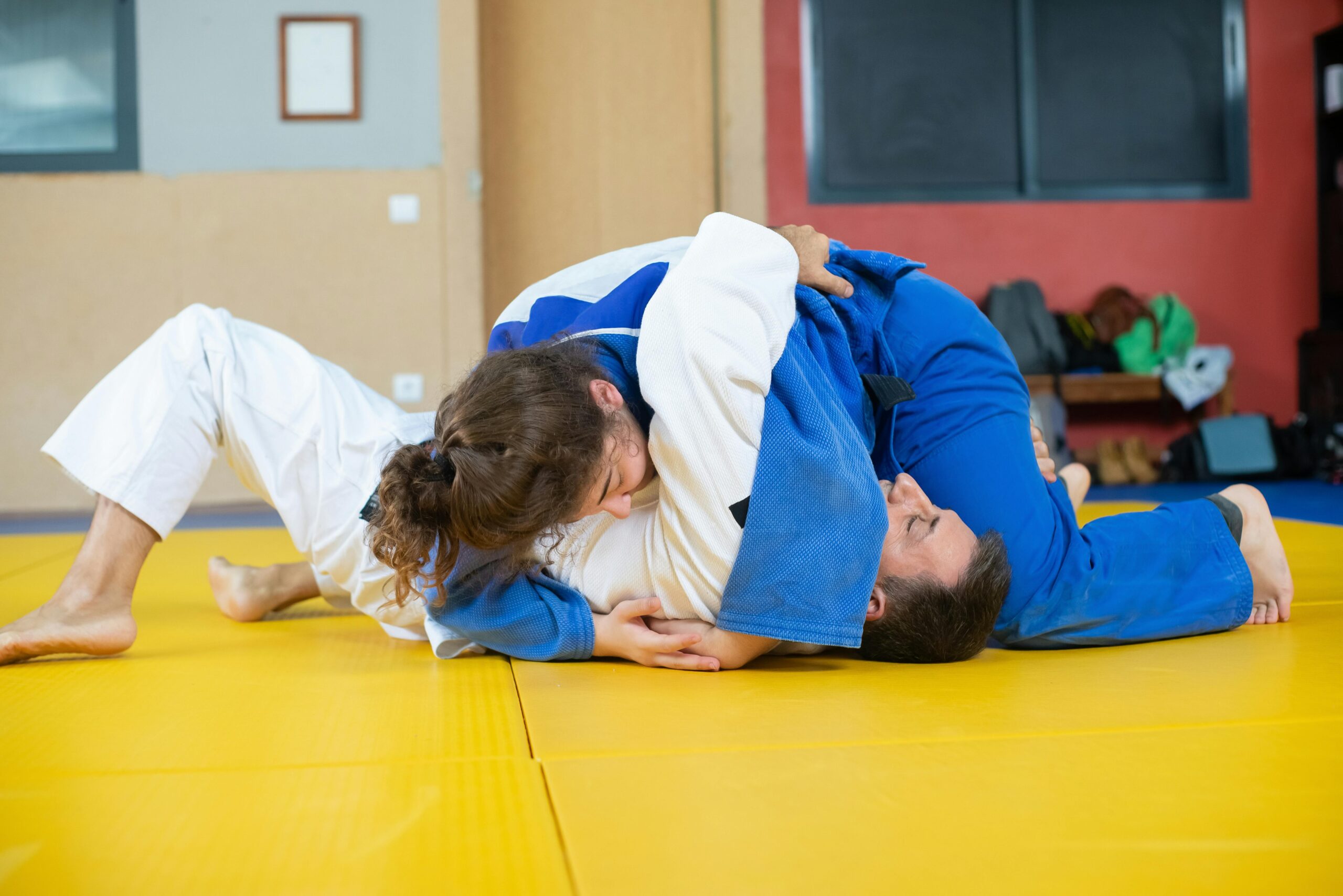 Two judokas practicing grappling techniques indoors during a judo training session.